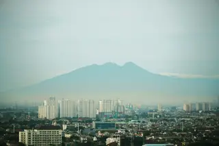 Ilustrasi: Pemandangan lanskap kota dengan latar belakang pegunungan di kejauhan.