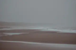 Ilustrasi: Pemandangan garis pantai berpasir yang diselimuti kabut tebal dan deburan ombak.