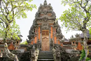 Ilustrasi: Gerbang candi tradisional Bali dengan ukiran batu berlatar pepohonan hijau.