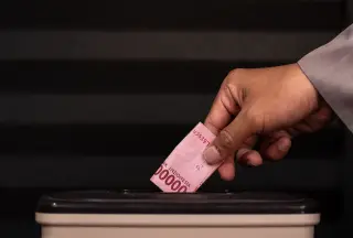 Ilustrasi: Tangan seseorang memasukkan uang kertas seratus ribu rupiah ke dalam kotak amal.