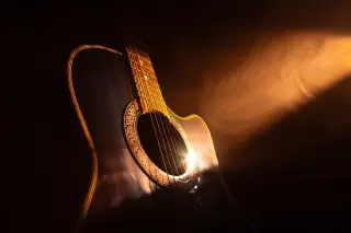 Ilustrasi: Gitar akustik disorot cahaya hangat dramatis berlatar belakang gelap dan berasap.