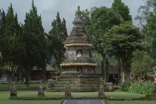 Ilustrasi: Stupa batu kuno di halaman pura dengan pepohonan hijau di sekelilingnya.
