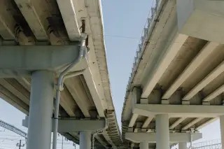 Ilustrasi: Struktur beton jalan layang dan pilar penyangga dengan latar langit cerah.