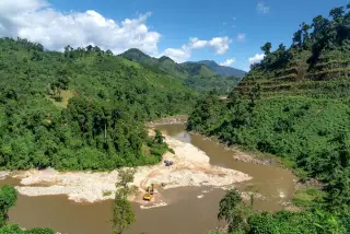 Ilustrasi: Alat berat ekskavator beroperasi di endapan pasir aliran sungai di antara perbukitan hijau.