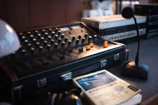 Ilustrasi: Mixer audio analog, mikrofon kecil, dan buku di atas meja kerja studio rekaman.