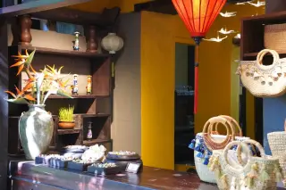 Ilustrasi: Deretan tas anyaman, perhiasan, dan dekorasi lampion dipajang di atas meja toko suvenir.