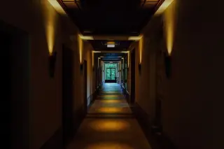 Ilustrasi: Sebuah lorong panjang temaram dengan pencahayaan lampu dinding yang dramatis.