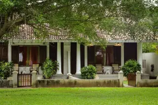 Ilustrasi: Rumah bergaya kolonial dengan halaman berumput hijau dan pepohonan rindang.