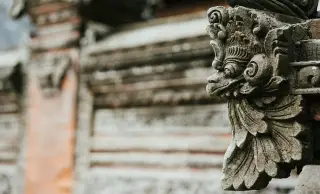 Ilustrasi: Ukiran batu tradisional khas Bali pada dinding pura dengan latar belakang buram.