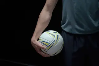 Ilustrasi: Seorang pria memegang bola voli dengan latar belakang gelap.