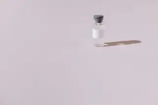 Ilustrasi: Sebuah botol kecil vial vaksin bening dengan label putih di atas permukaan polos.