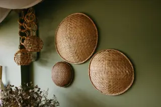 Ilustrasi: Beberapa kerajinan anyaman bambu berbentuk bulat dan lampion tergantung di dinding hijau.
