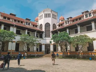 Ilustrasi: Halaman gedung bersejarah Lawang Sewu dengan beberapa orang berjalan di bawah langit cerah.