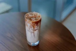 Ilustrasi: Segelas minuman es kopi susu di atas meja kayu dengan latar belakang kabur.
