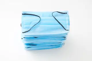 Ilustrasi: Tumpukan masker medis sekali pakai berwarna biru di atas latar belakang putih.