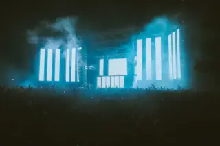 Ilustrasi: Kerumunan penonton menyaksikan konser musik dengan panggung besar berlayar LED bercahaya terang.