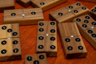 Ilustrasi: Sejumlah bidak domino kayu tersusun di atas permukaan meja kayu.