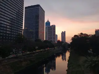 Ilustrasi: Pemandangan gedung-gedung bertingkat di tepi sungai dengan latar langit senja di Jakarta.