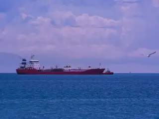 Ilustrasi: Kapal tanker merah berlayar di laut lepas berlatar awan mendung.