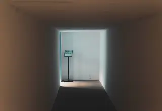 Ilustrasi: Lorong kosong berdinding polos dengan papan petunjuk kecil di ujung yang terang.