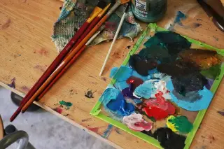 Ilustrasi: Palet berisi cat warna-warni dan beberapa kuas lukis di atas meja kayu.