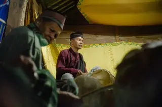 Ilustrasi: Beberapa pria memainkan alat musik tradisional gendang di dalam ruangan berhias kain kuning.