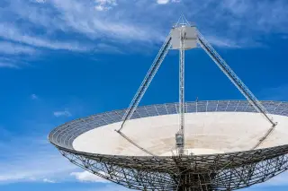 Ilustrasi: Antena parabola komunikasi satelit berukuran besar dengan latar belakang langit biru berawan tipis.