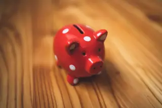 Ilustrasi: Celengan berbentuk babi berwarna merah dengan motif polkadot putih di atas meja kayu.