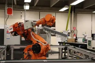 Ilustrasi: Lengan robot industri berwarna jingga beroperasi di dalam ruang laboratorium otomasi.