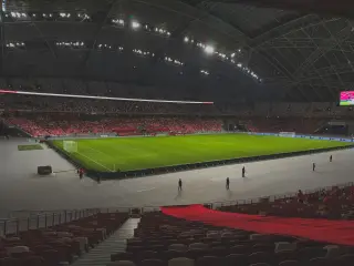 Ilustrasi: Pemandangan dalam stadion sepak bola berkubah besar dengan lapangan hijau dan tribun penonton.