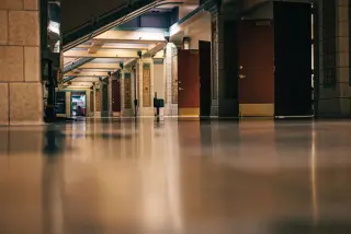 Ilustrasi: Lantai lorong gedung yang mengilap memantulkan cahaya di samping deretan pintu kayu.
