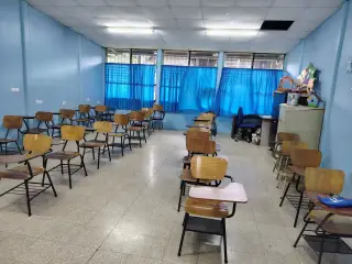 Ilustrasi: Deretan kursi kuliah kayu di dalam ruang kelas kosong berdinding biru.