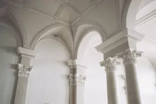 Ilustrasi: Interior ruangan megah dengan pilar dan lengkungan berornamen arsitektur klasik.