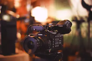 Ilustrasi: Kamera video profesional terpasang di atas tripod dalam ruangan studio berlatar buram.