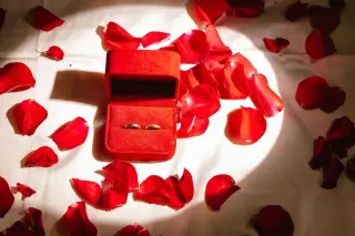Ilustrasi: Dua cincin di dalam kotak merah beludru yang dikelilingi kelopak mawar merah.