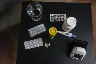 Ilustrasi: Aneka obat-obatan, termometer digital, tensimeter, dan segelas air di atas meja hitam.