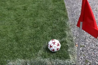 Ilustrasi: Sebuah bola sepak berada di sudut lapangan rumput dekat bendera merah.