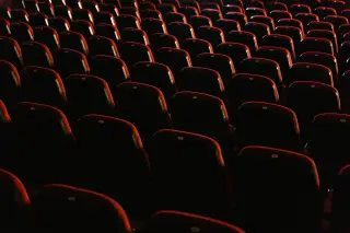 Ilustrasi: Deretan kursi teater berwarna merah yang kosong dalam pencahayaan redup.