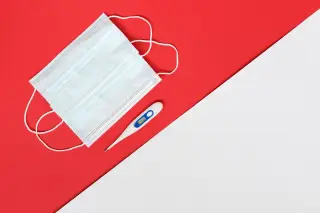 Ilustrasi: Masker medis dan termometer digital di atas latar belakang merah dan putih.