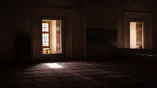 Ilustrasi: Interior masjid sunyi dengan cahaya matahari menyinari karpet bermotif dan dinding batu berkaligrafi.