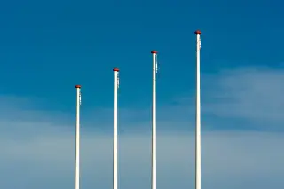 Ilustrasi: Empat tiang bendera putih berdiri berjajar dengan latar langit biru cerah.