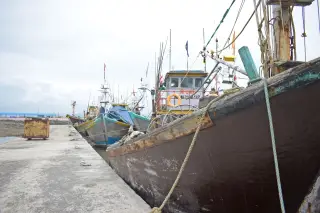 Ilustrasi: Deretan kapal nelayan kayu bersandar di dermaga beton pelabuhan.