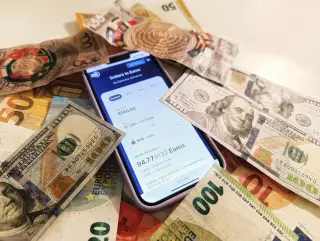 Ilustrasi: Ponsel menampilkan aplikasi konversi kurs di antara beberapa lembar uang kertas asing.