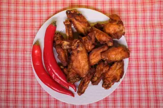 Ilustrasi: Sepiring sayap ayam goreng dan cabai merah di atas taplak meja bermotif kotak-kotak.