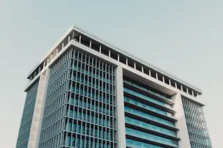 Ilustrasi: Sudut pandang bawah dari gedung perkantoran modern bertingkat dengan fasad kaca dan kisi-kisi.