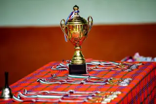 Ilustrasi: Piala berwarna emas dan sejumlah medali di atas meja beralas kain motif kotak-kotak merah.