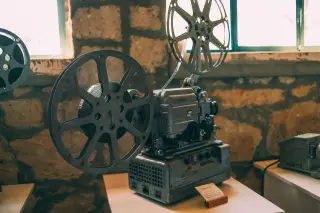 Ilustrasi: Proyektor film antik dengan roda pita seluloid dipajang di atas meja.