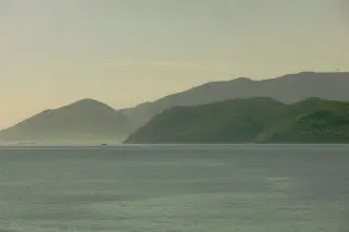 Ilustrasi: Pemandangan laut tenang dengan deretan bukit di kejauhan berselimut kabut.