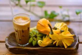 Ilustrasi: Segelas es kopi berbusa dan beberapa labu hias di atas nampan kayu.