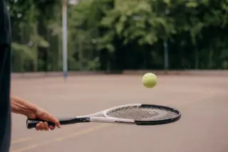 Ilustrasi: Tangan seseorang memegang raket tenis dengan bola tenis melayang di atasnya.